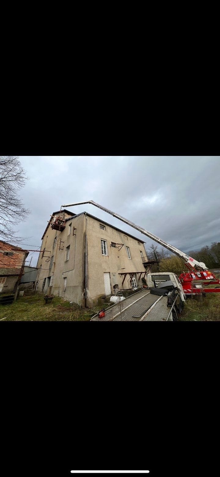Camion-grue et nacelle contre un bâtiment de trois étages pendant la démolition de sa toiture, à Combronde